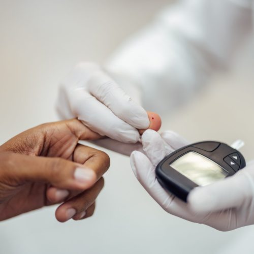 Measuring blood sugar level with blood glucose meter. Hands of a patient and medical worker in gloves holding medical instrument.