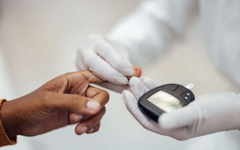 Measuring blood sugar level with blood glucose meter. Hands of a patient and medical worker in gloves holding medical instrument.
