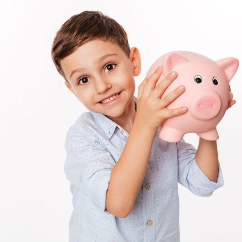 Close up portrait of a cheerful cute little kid holding piggy bank and looking at camera isolated over white background